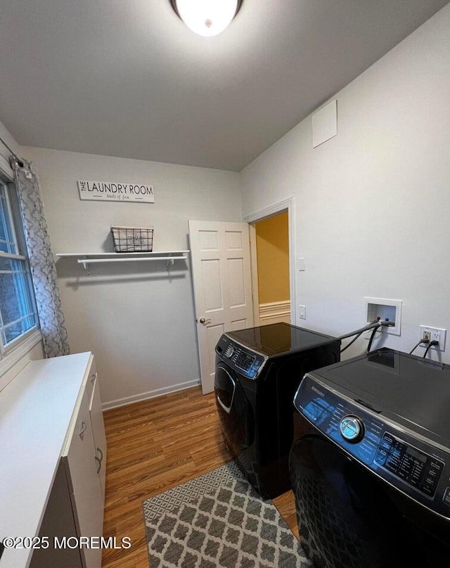 clothes washing area with baseboards, washing machine and clothes dryer, cabinet space, and wood finished floors
