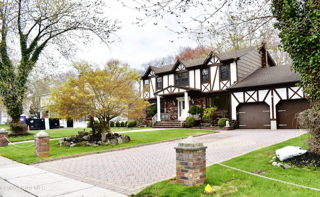 tudor house with an attached garage, roof with shingles, a front lawn, and decorative driveway