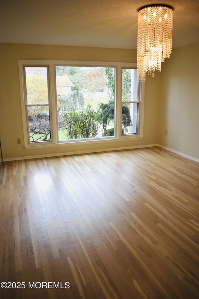 unfurnished room with baseboards, a notable chandelier, and wood finished floors