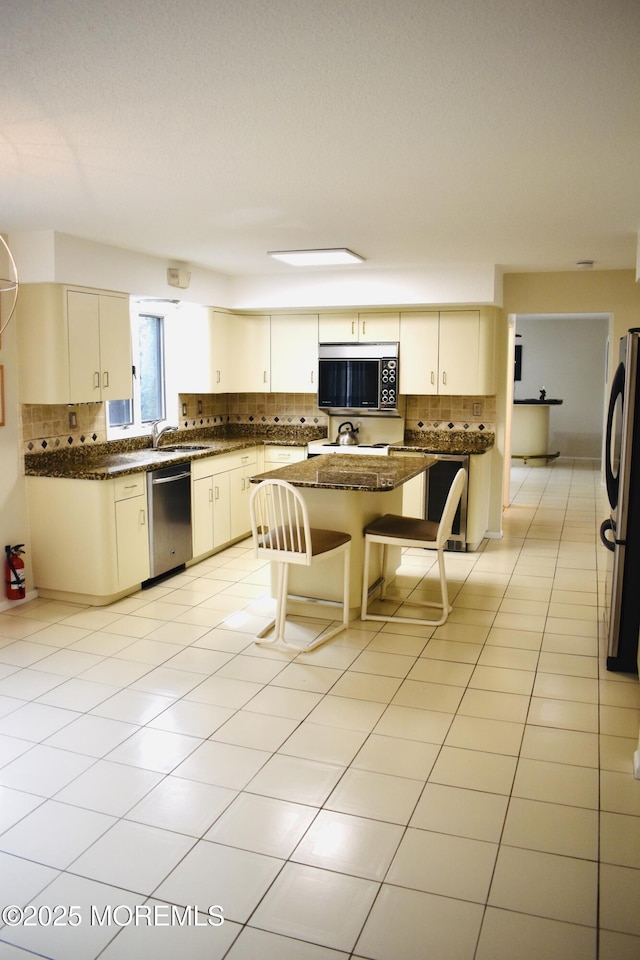 kitchen featuring tasteful backsplash, light tile patterned floors, a center island, stainless steel appliances, and a sink