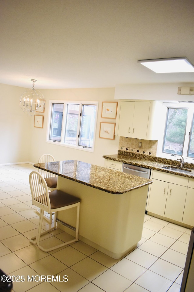 kitchen with tasteful backsplash, a notable chandelier, dark stone countertops, light tile patterned floors, and a sink