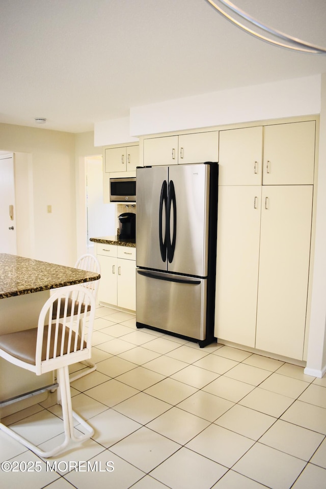 kitchen featuring dark stone countertops, cream cabinets, light tile patterned flooring, and appliances with stainless steel finishes