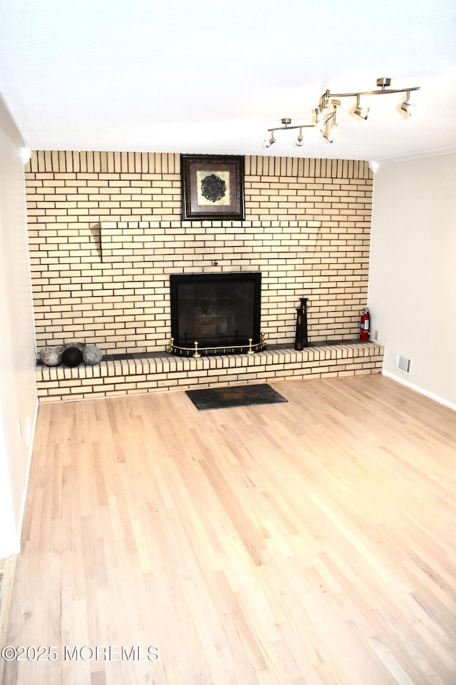unfurnished living room with wood finished floors, visible vents, baseboards, and a brick fireplace