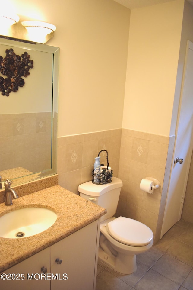 half bathroom with toilet, tile walls, a wainscoted wall, vanity, and tile patterned floors