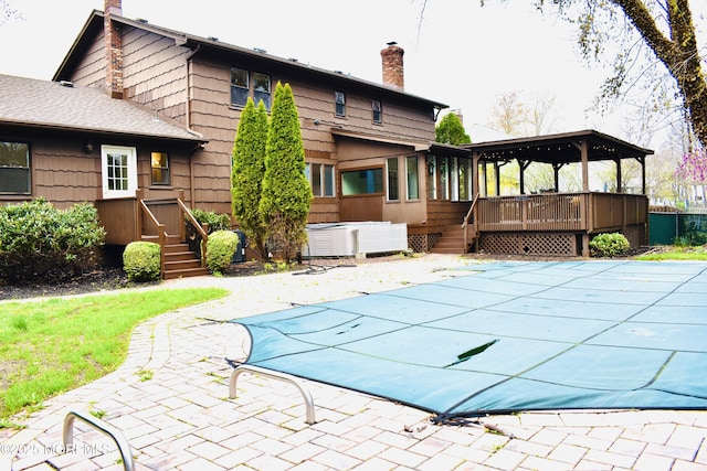 rear view of house featuring a fenced in pool, a chimney, a patio area, a hot tub, and a deck