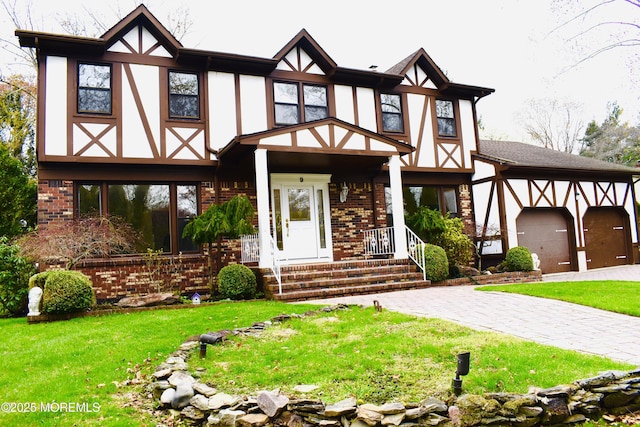 english style home featuring a front yard, brick siding, stucco siding, and decorative driveway