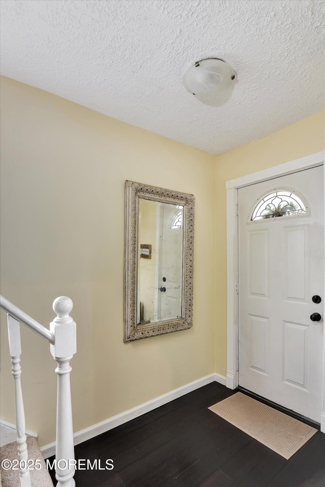 foyer entrance featuring a textured ceiling, baseboards, and dark wood-style floors