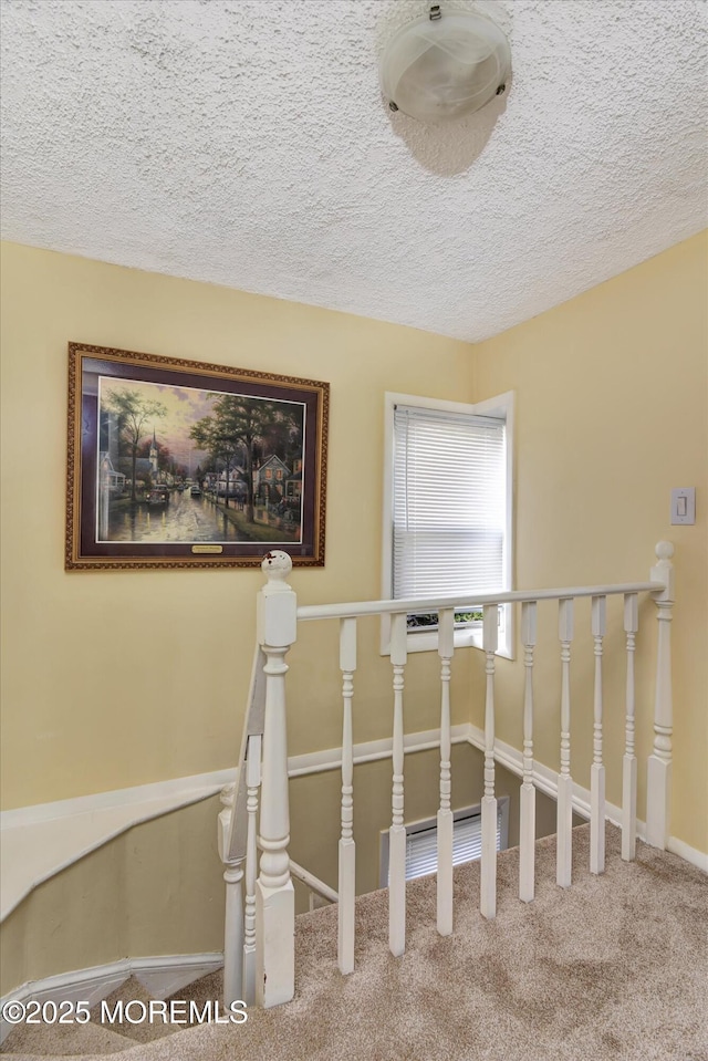 staircase with a textured ceiling, baseboards, and carpet floors