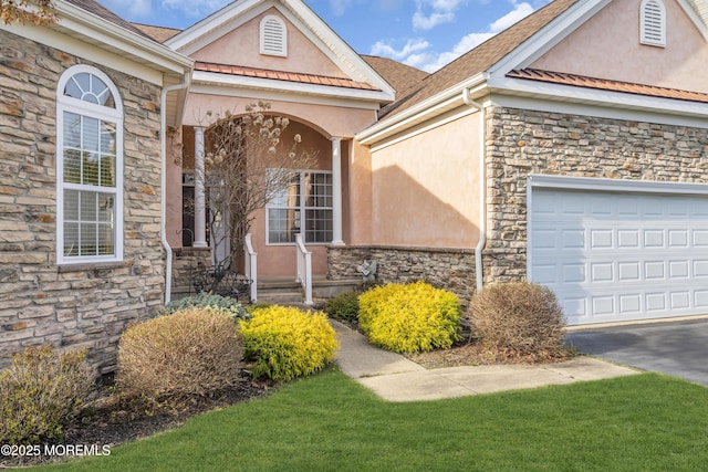 view of exterior entry with stone siding, a garage, and stucco siding