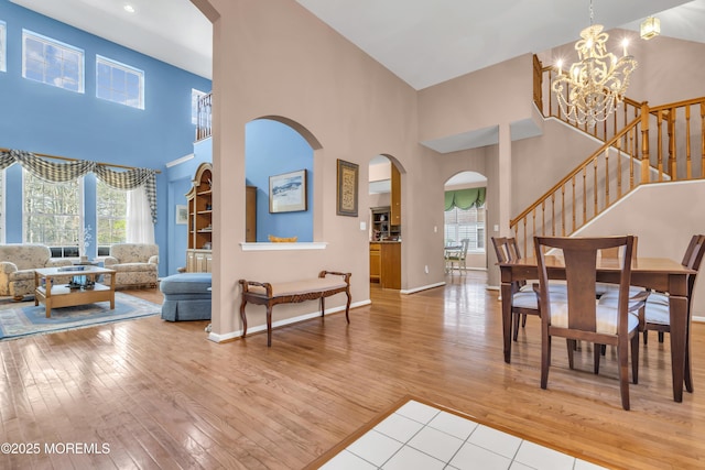 foyer entrance featuring arched walkways, a high ceiling, a chandelier, light wood finished floors, and stairs