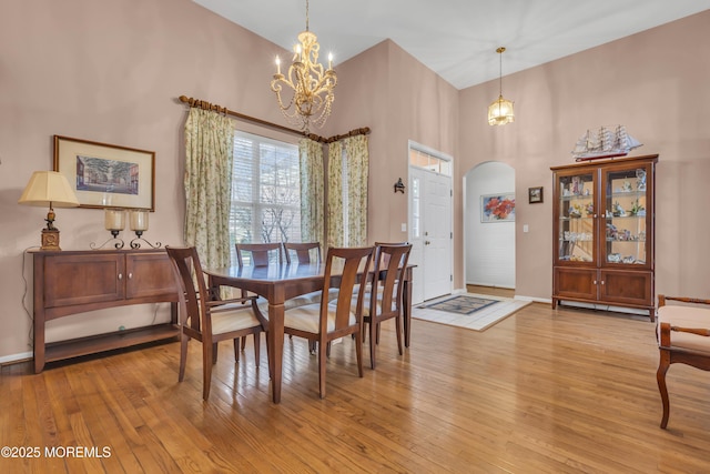 dining space with a notable chandelier, baseboards, light wood-style flooring, a high ceiling, and arched walkways