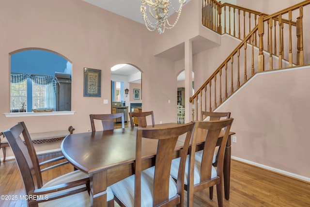 dining space featuring arched walkways, a chandelier, wood finished floors, a high ceiling, and stairs