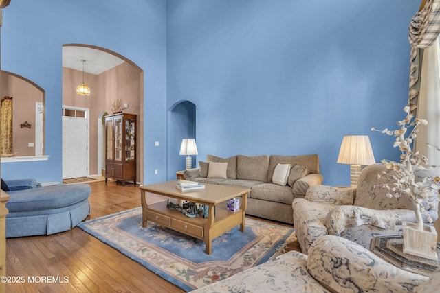 living area featuring baseboards, arched walkways, hardwood / wood-style floors, and a towering ceiling