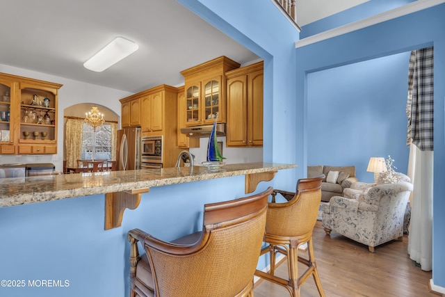 kitchen featuring a breakfast bar, a chandelier, glass insert cabinets, under cabinet range hood, and appliances with stainless steel finishes