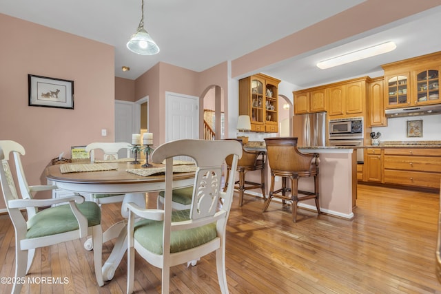 dining space with arched walkways and light wood-type flooring