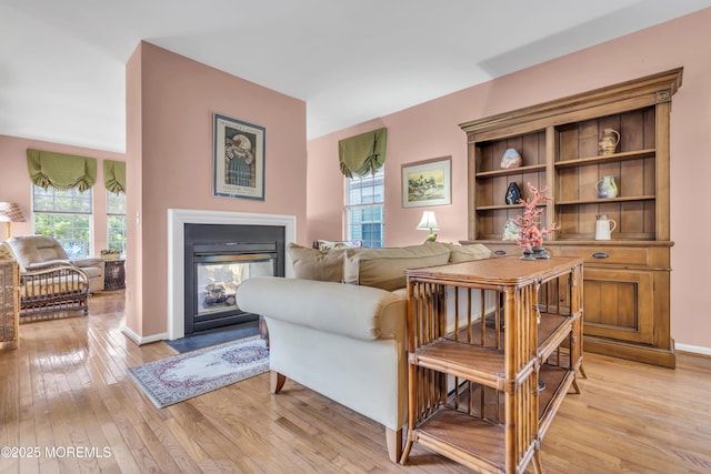 living area with light wood finished floors, baseboards, and a multi sided fireplace