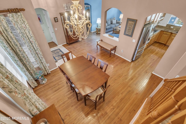 dining room with arched walkways, light wood finished floors, baseboards, and an inviting chandelier