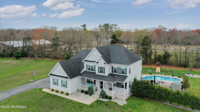 exterior space with a shingled roof, a fenced in pool, covered porch, and a yard