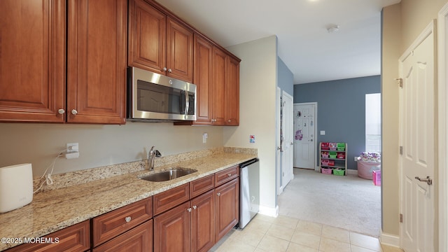 kitchen with stainless steel appliances, light tile patterned floors, a sink, light stone countertops, and light colored carpet