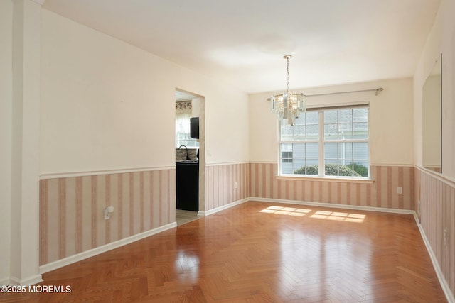 empty room featuring baseboards, an inviting chandelier, wainscoting, and a sink