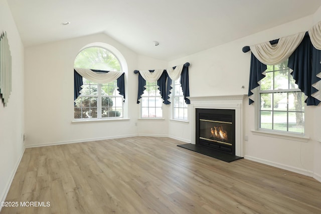 unfurnished living room featuring vaulted ceiling, plenty of natural light, wood finished floors, and a glass covered fireplace