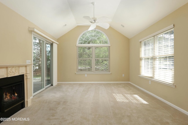 unfurnished living room featuring plenty of natural light, carpet flooring, ceiling fan, and a lit fireplace