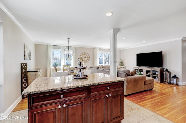 kitchen featuring dark brown cabinets, decorative light fixtures, light stone countertops, crown molding, and decorative columns