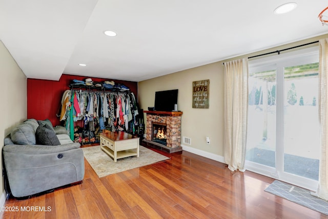living room featuring baseboards, visible vents, recessed lighting, wood finished floors, and a stone fireplace
