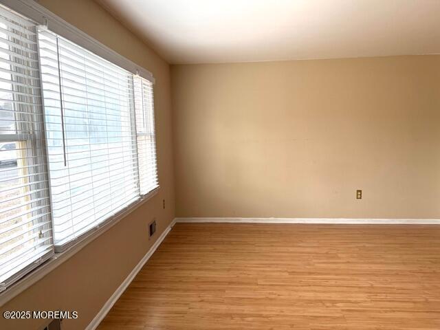 empty room with visible vents, light wood-type flooring, and baseboards