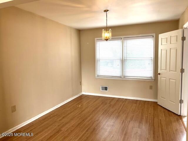 unfurnished dining area featuring wood finished floors, an inviting chandelier, baseboards, and visible vents
