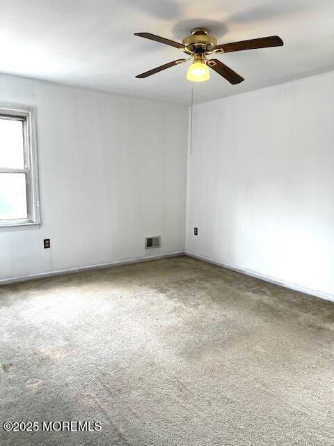 carpeted spare room with baseboards, a ceiling fan, and visible vents