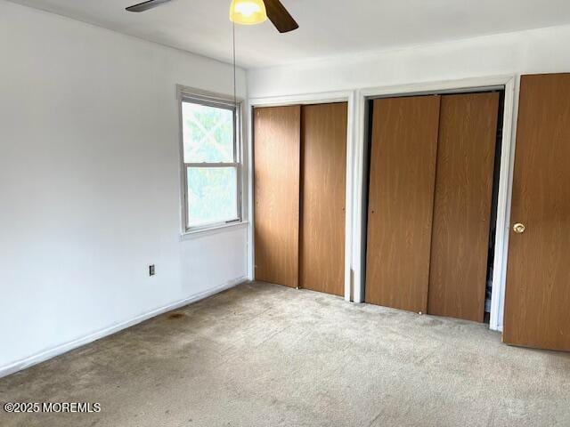 unfurnished bedroom with two closets, carpet flooring, and ceiling fan
