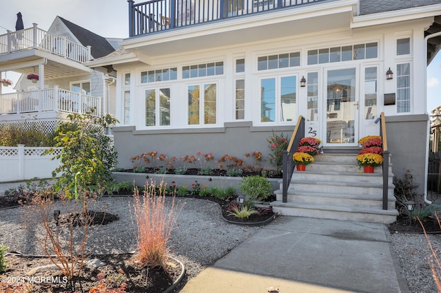 doorway to property with stucco siding, fence, a balcony, and a shingled roof