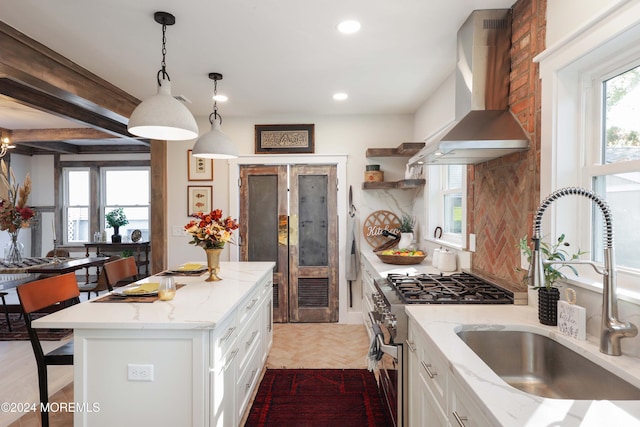 kitchen with high end stainless steel range, wall chimney exhaust hood, a sink, white cabinetry, and open shelves