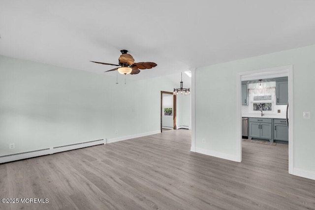 unfurnished living room featuring light wood finished floors, a sink, a baseboard heating unit, baseboards, and ceiling fan with notable chandelier