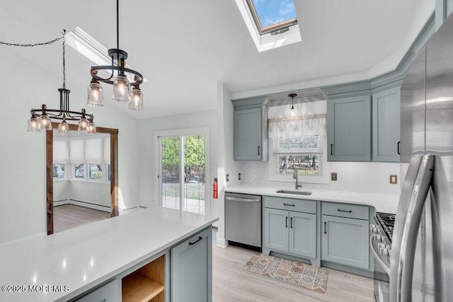 kitchen with light countertops, a sink, light wood-style flooring, tasteful backsplash, and appliances with stainless steel finishes