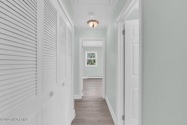 hall with light wood-type flooring, baseboard heating, and baseboards