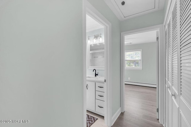 corridor with light wood-type flooring, baseboard heating, and a sink