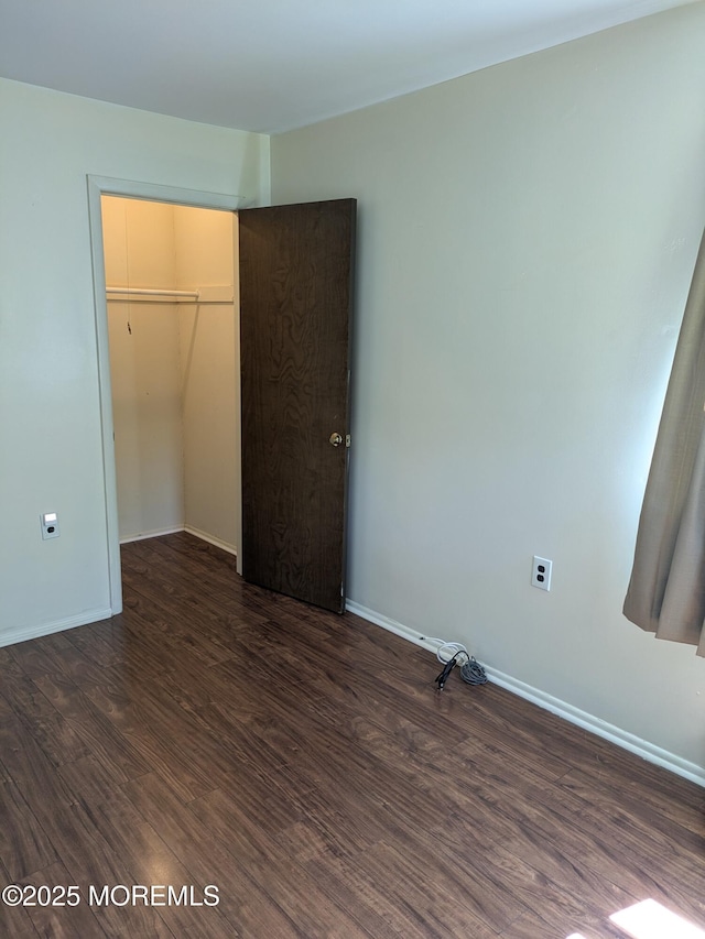 unfurnished bedroom with baseboards, dark wood-style flooring, and a closet