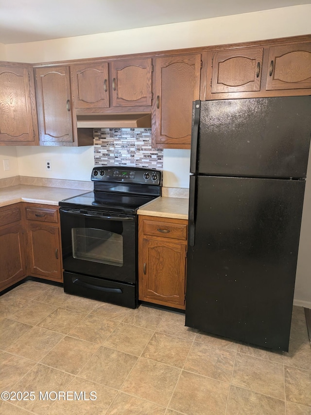 kitchen featuring tasteful backsplash, brown cabinets, light countertops, black appliances, and under cabinet range hood