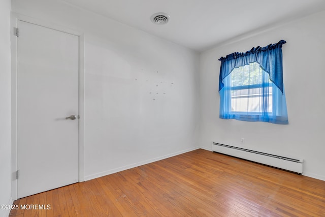 spare room featuring visible vents, baseboards, wood-type flooring, and a baseboard heating unit