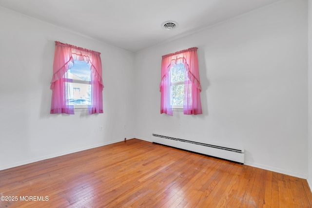 empty room featuring baseboards, a baseboard heating unit, visible vents, and light wood-type flooring
