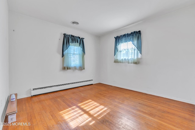 unfurnished room featuring visible vents, baseboards, wood-type flooring, and a baseboard heating unit