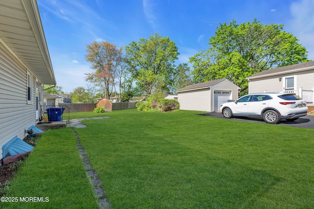 view of yard featuring a detached garage, fence, and an outbuilding