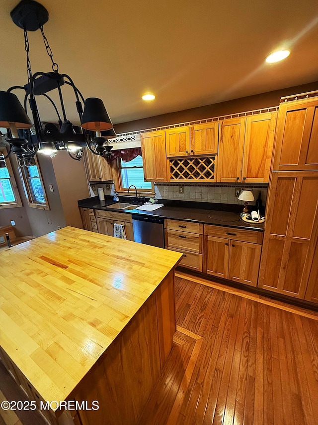 kitchen featuring dishwasher, a sink, an inviting chandelier, wood counters, and dark wood-type flooring