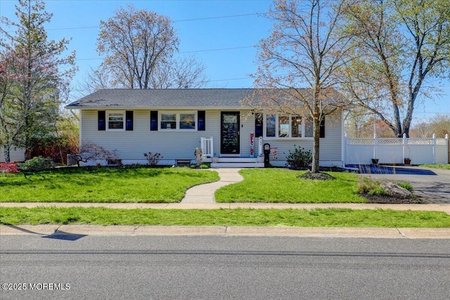 ranch-style home featuring a front lawn, fence, and roof with shingles
