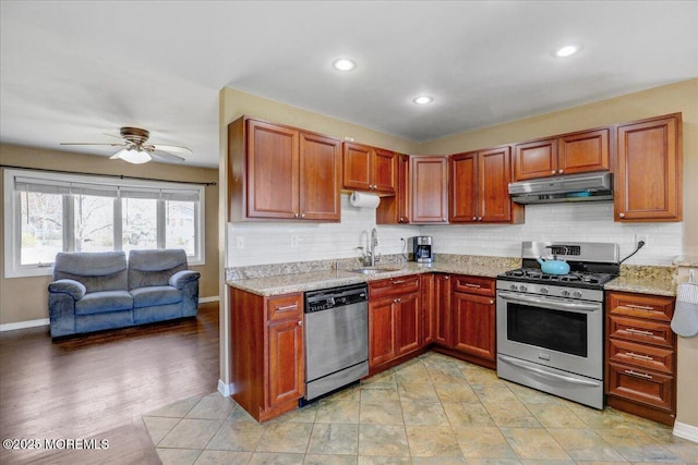 kitchen featuring backsplash, appliances with stainless steel finishes, under cabinet range hood, and a sink