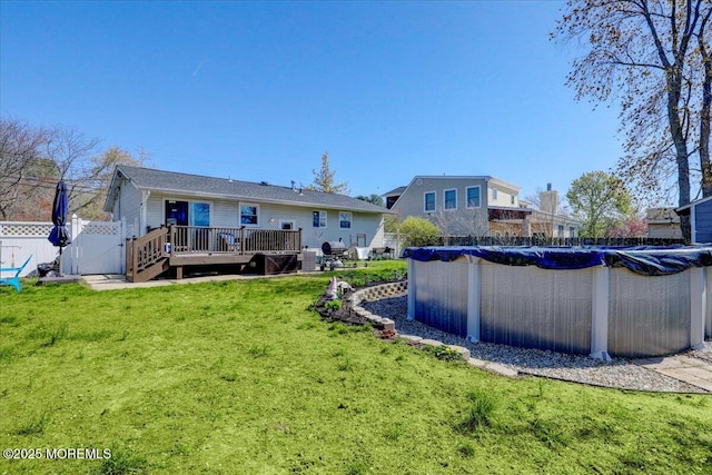 back of house featuring a gate, fence, a wooden deck, a lawn, and a covered pool