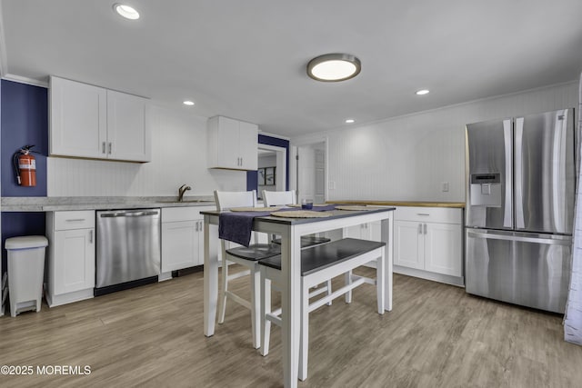 kitchen with crown molding, light wood-style flooring, appliances with stainless steel finishes, and white cabinetry