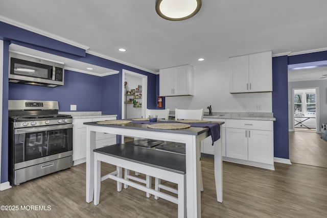 kitchen with white cabinets, recessed lighting, wood finished floors, ornamental molding, and appliances with stainless steel finishes